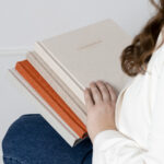 Femme tenant plusieurs albums photo artisanaux, avec couverture en lin et dorure, fabriqués au Luxembourg