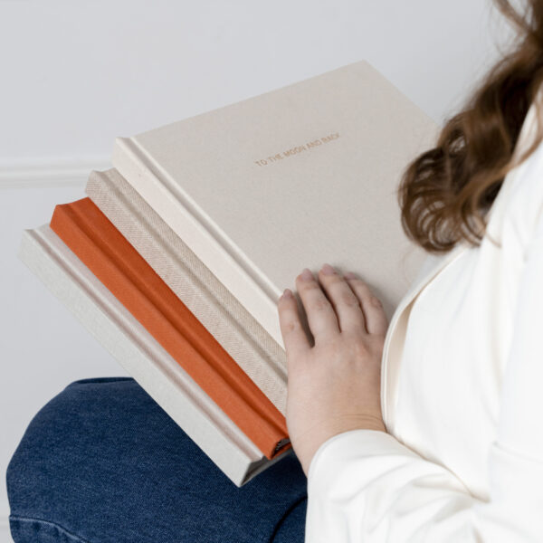 Femme tenant plusieurs albums photo artisanaux, avec couverture en lin et dorure, fabriqués au Luxembourg