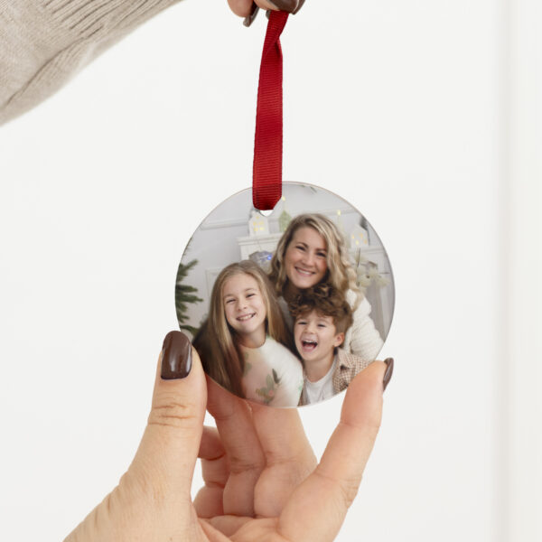 Ornement de Noël personnalisé en verre avec photo de famille et ruban rouge, tenu à la main.