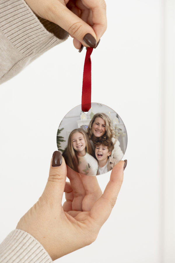 Ornement de Noël personnalisé en verre avec photo de famille et ruban rouge, tenu à la main.
